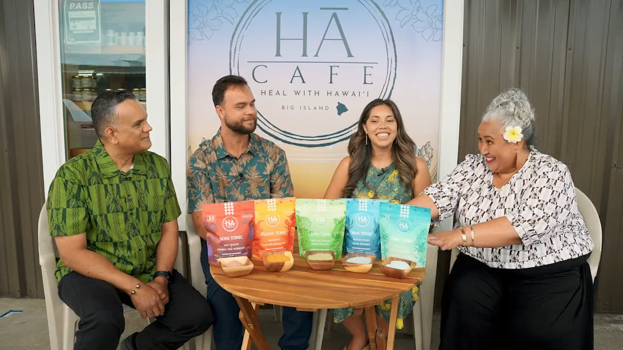 Four people sit in front of a HĀ Cafe sign with four colorful bags of products displayed on a table between them.